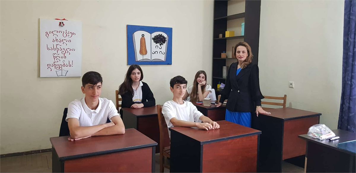 მოსწავლეები და მასწავლებელი ახალი სასწავლო წლის მისალოც პლაკატთან